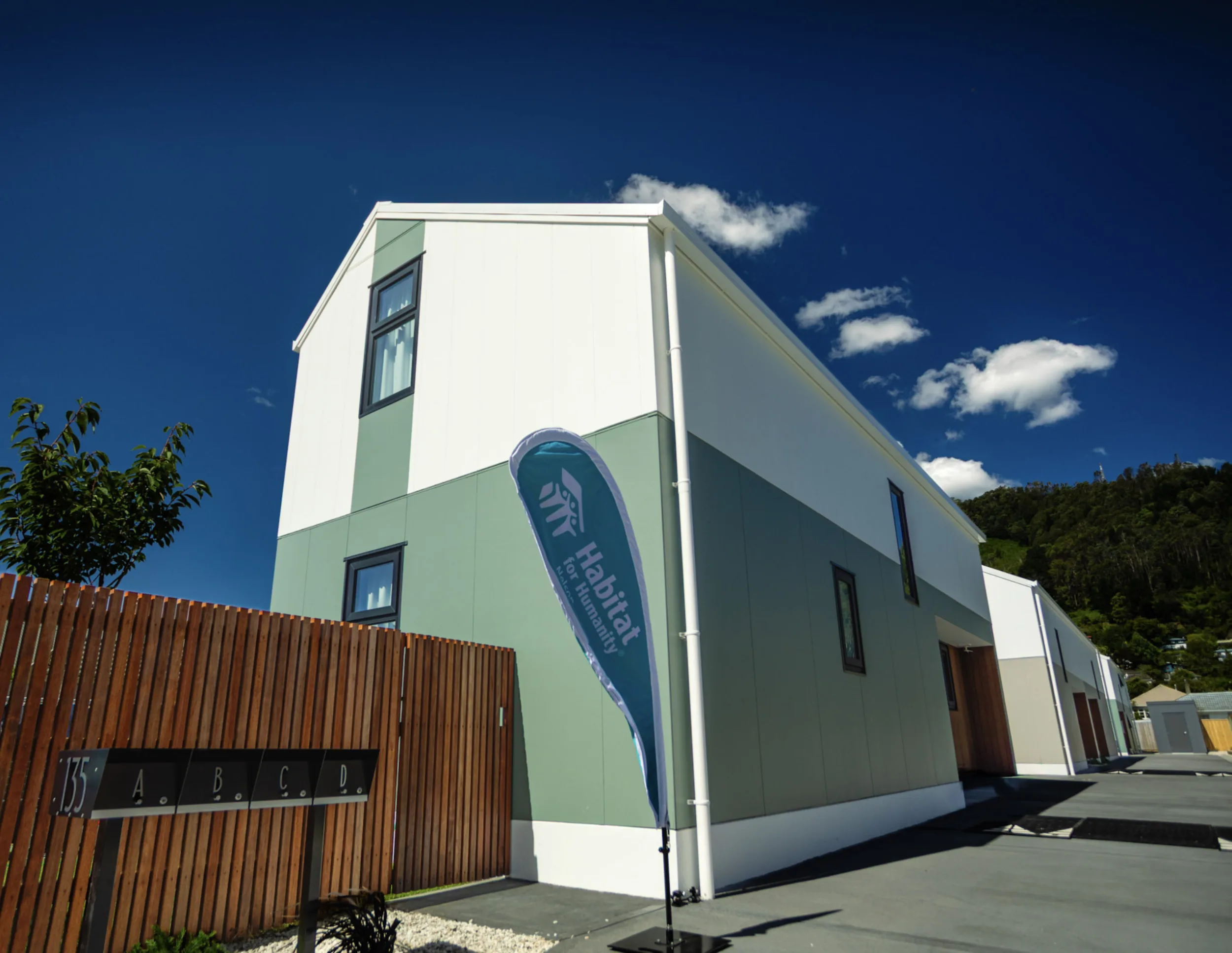 Exterior view of newly built Habitat Nelson townhouses with Habitat flag outside the development on a sunny day