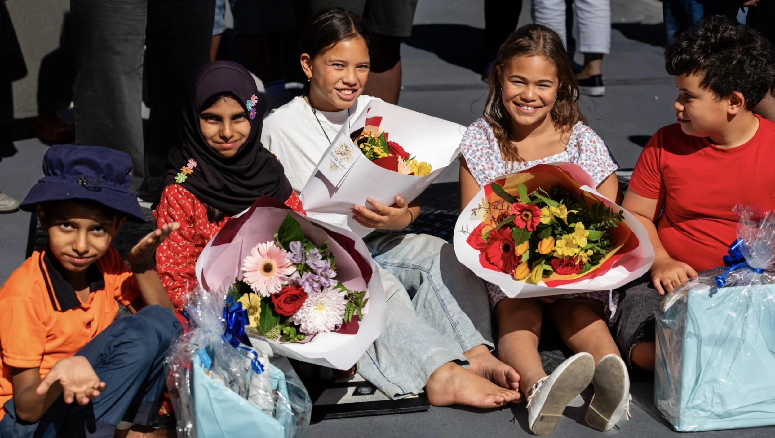 Four children sitting together holding bouquets and gift baskets during a Haitat Nelson housing dedication celebration
