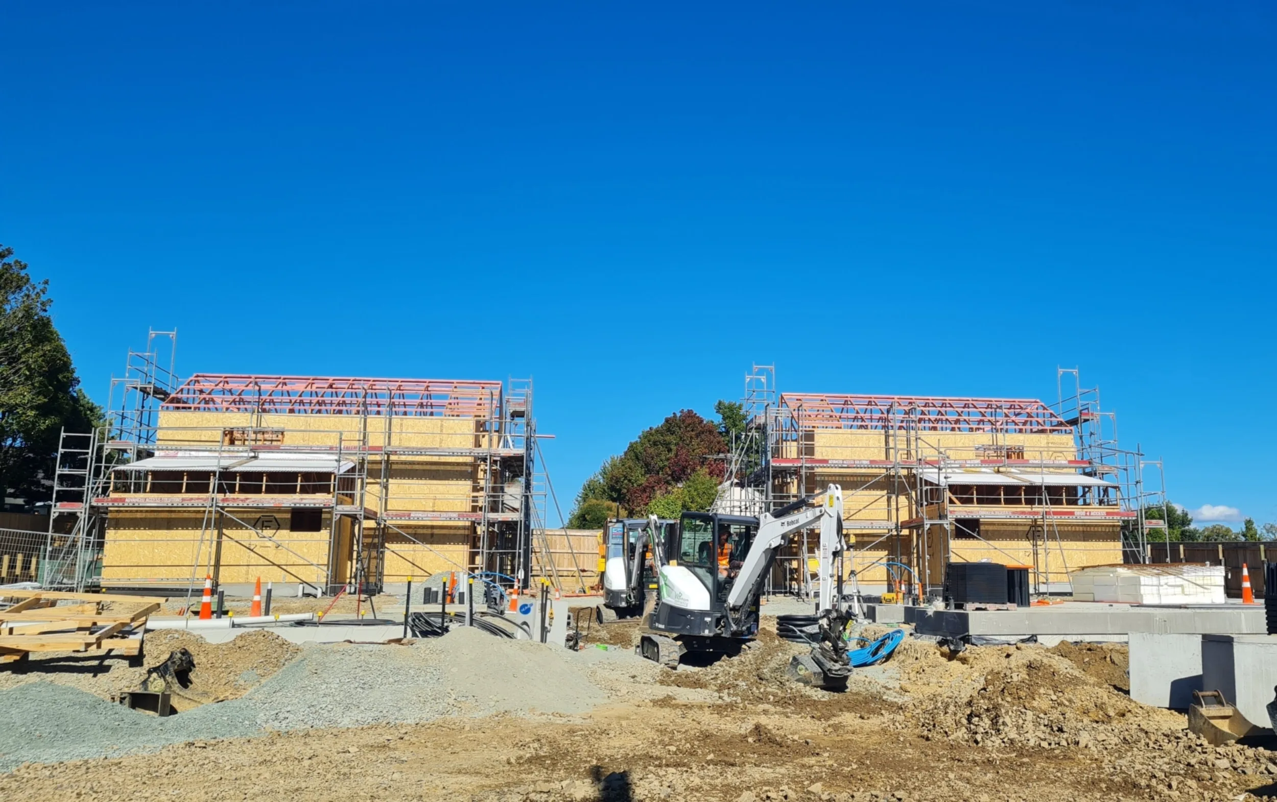 Construction underway on Habitat Nelson’s Richmond development, showing framed townhouses, scaffolding and excavators on site under a clear blue sky