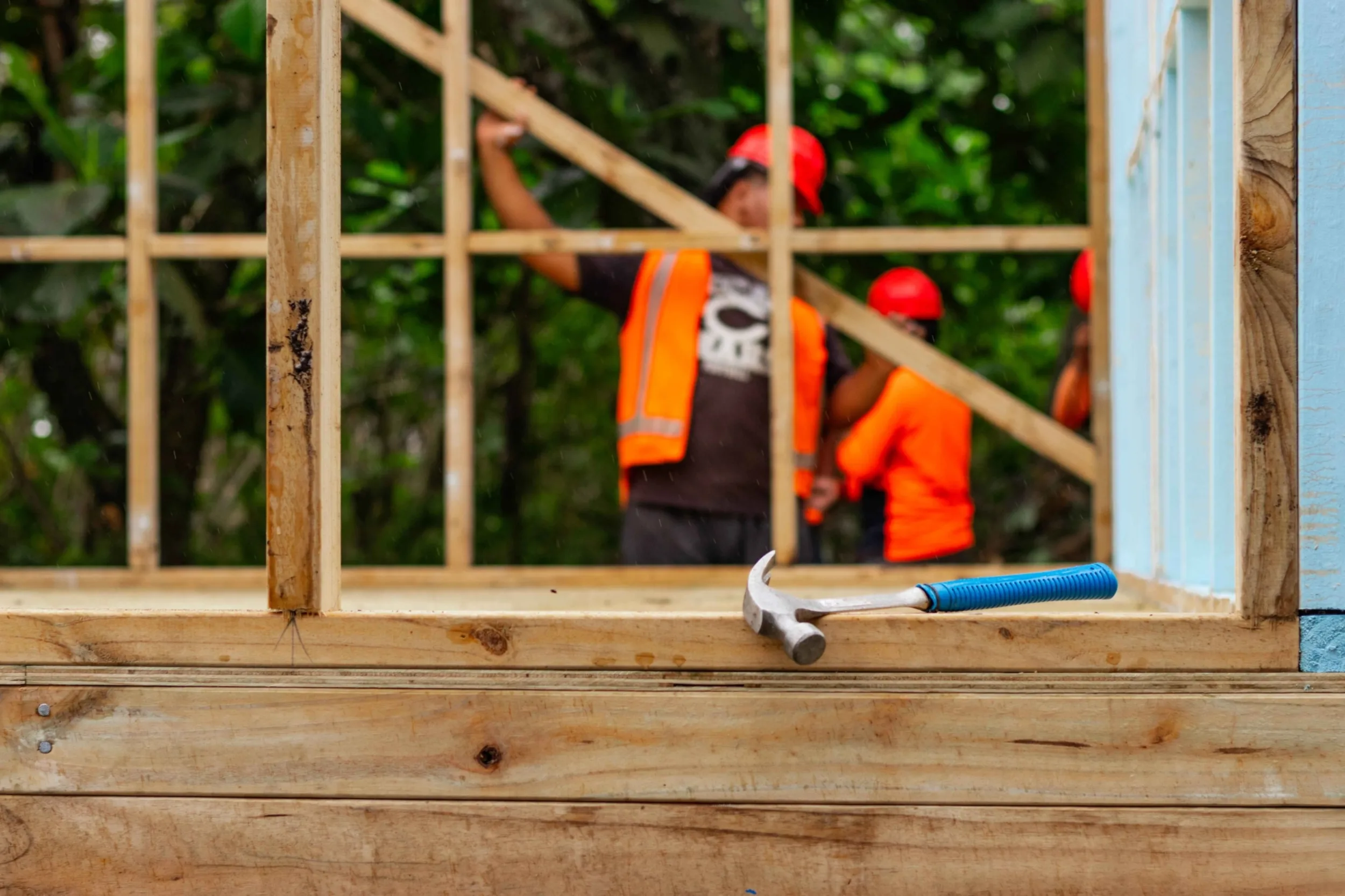 A house construction frame that was produced by the Build Back Safer Programme in Tonga. Several programme participants blurred in the background.